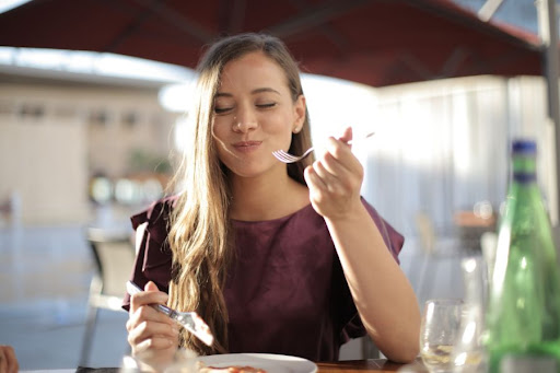 A woman eating outside at a bistro, seated under a an umbrella